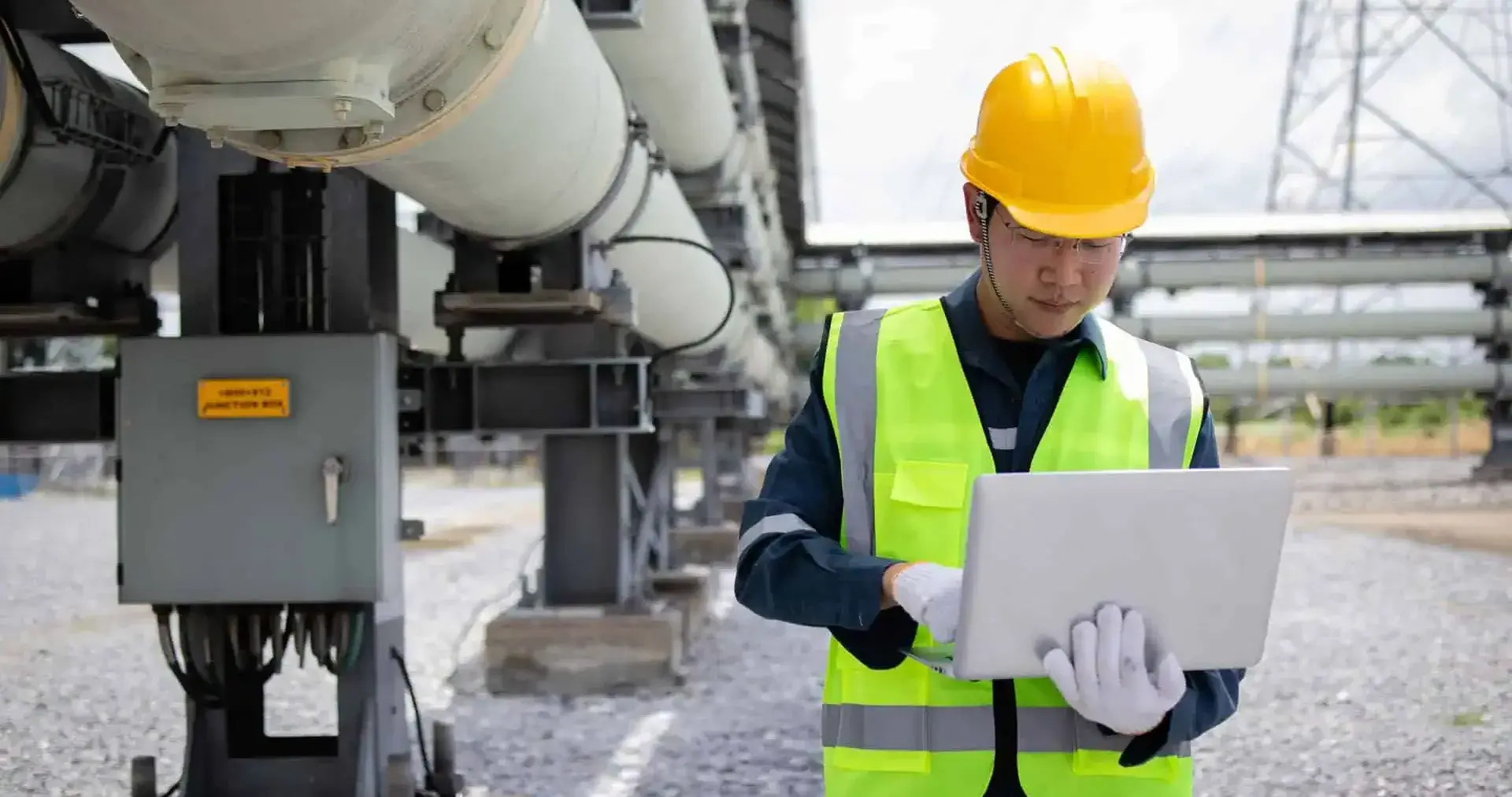 Utility worker using a laptop outdoors at an industrial location